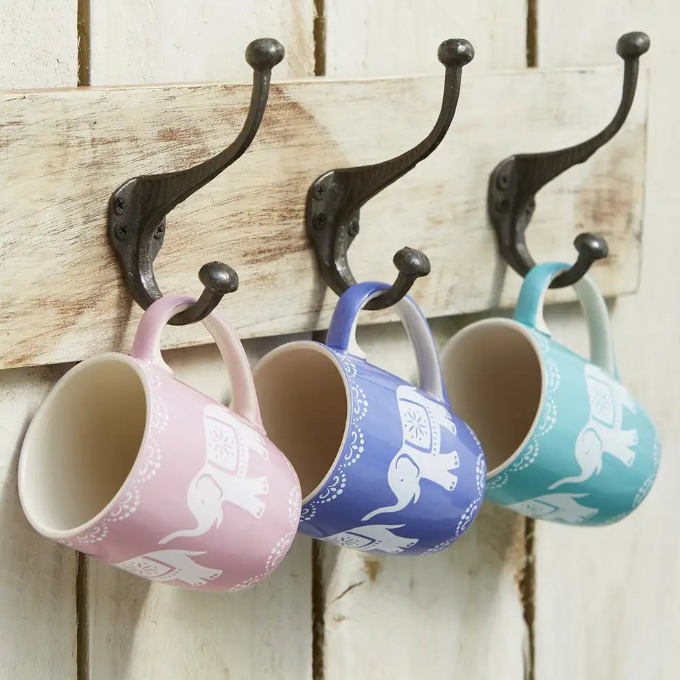 Three mugs hanging on a wooden board with metal hooks against a white background